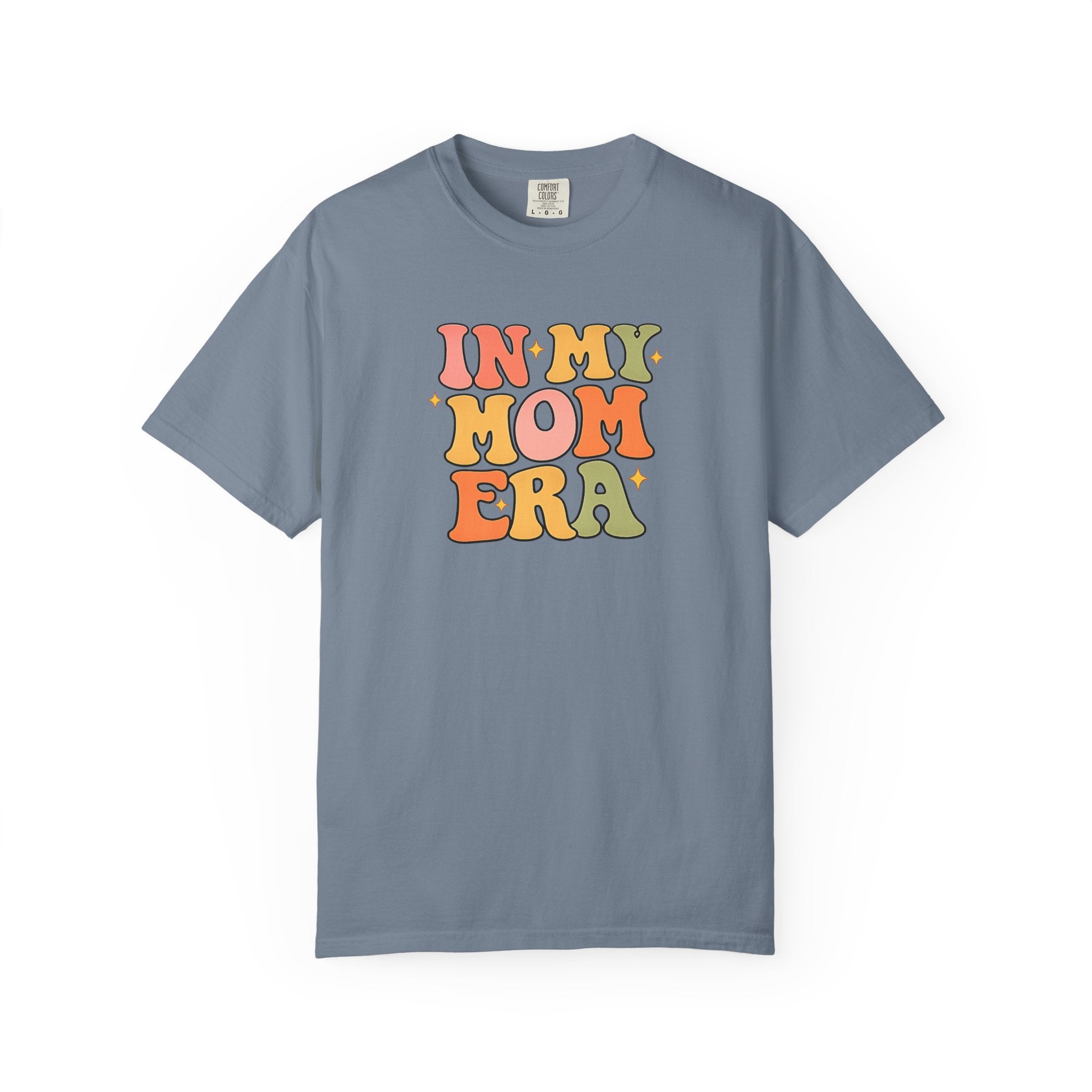 A slate blue short-sleeve t-shirt with a retro-style multicolor graphic on the chest that reads 'IN MY MOM ERA' in wavy, bubble letters.
