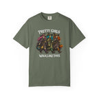 An olive green short-sleeve t-shirt with a graphic of four cartoon witch girls in colorful outfits, with the text 'PRETTY GIRLS WALK LIKE THIS' printed in white around the graphic.