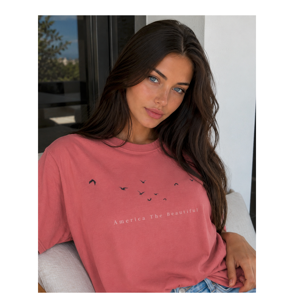 Woman wearing a pink t-shirt with text and graphics, sitting indoors.