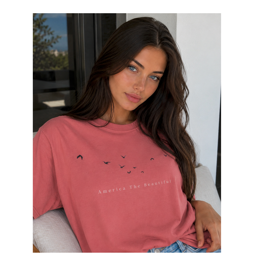 Woman wearing a pink t-shirt with text and graphics, sitting indoors.