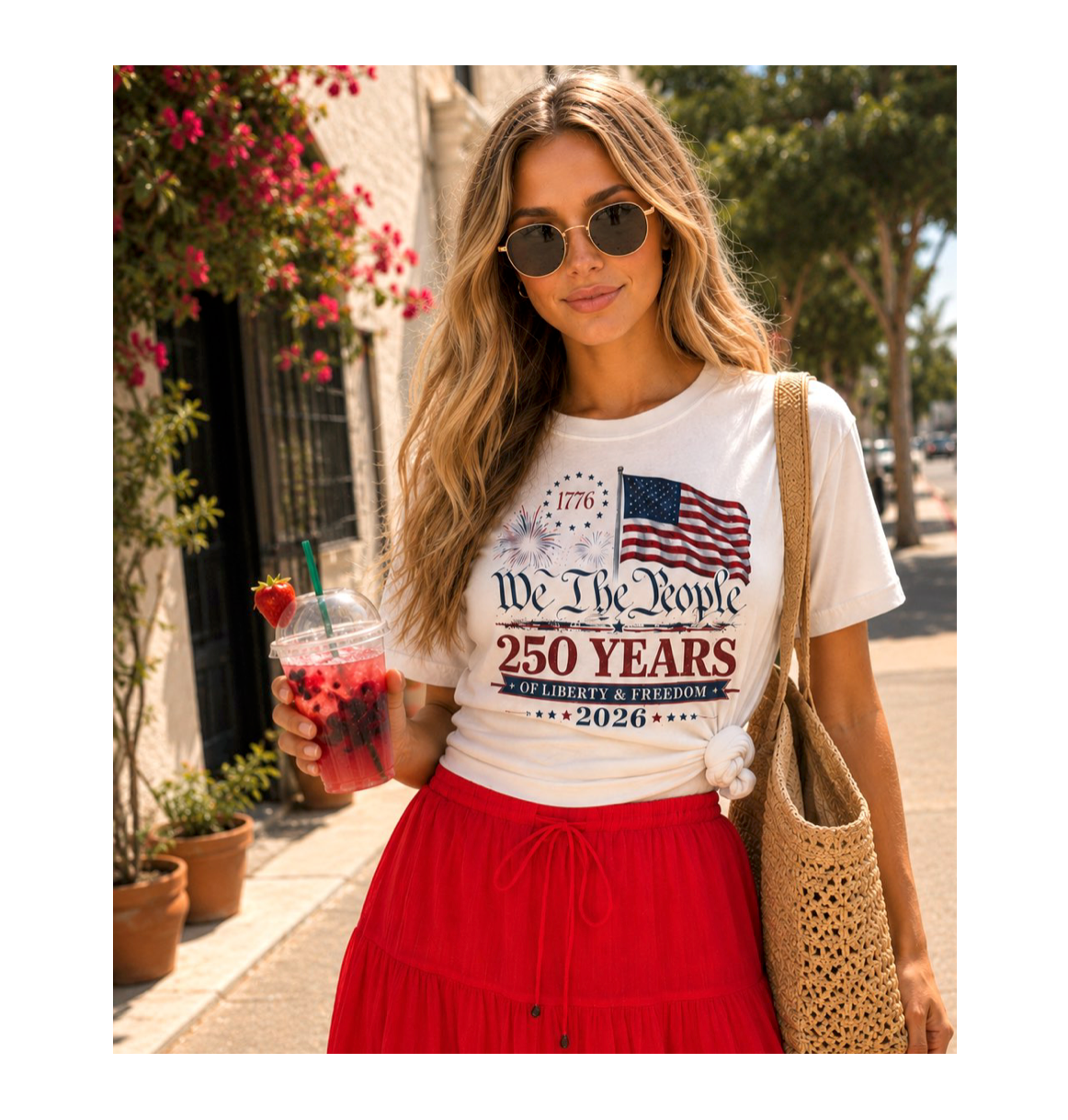 Woman wearing a white t-shirt with a patriotic design, holding a drink, and standing outdoors.