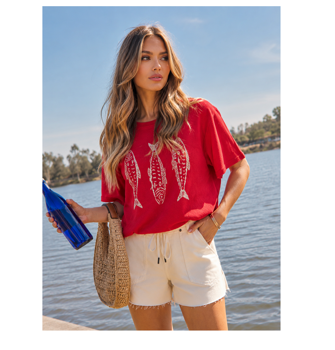 Woman in a red shirt with fish design by a body of water