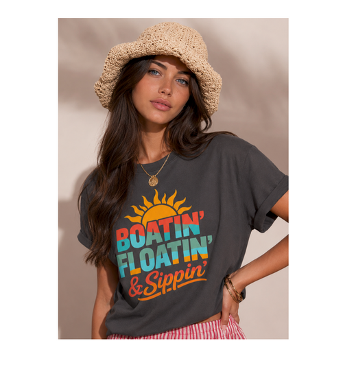 Woman wearing a gray t-shirt with colorful text and a sun graphic, standing against a plain background.