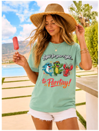 Woman wearing a light green t-shirt with cartoon characters and text, holding a popsicle outdoors.