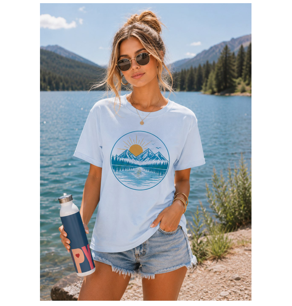 Woman wearing a white t-shirt with a mountain design by a lake