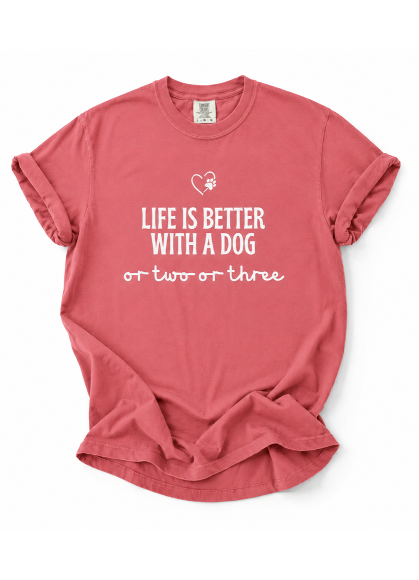 Pink t-shirt with 'Life is better with a dog or two or three' text on a white background