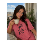 Woman in pink shirt with 'Coffee First' text holding a mug on a balcony.