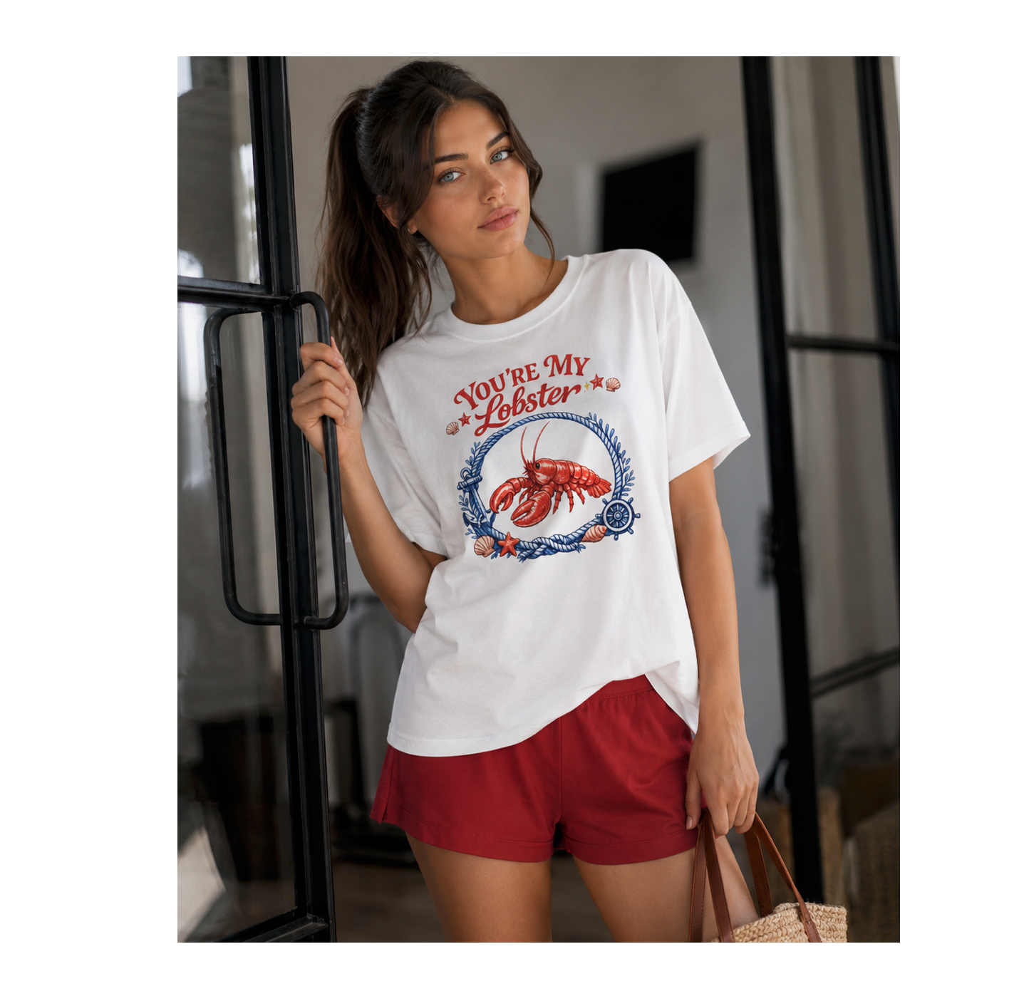 A woman wearing a white graphic t-shirt with a lobster design and the text 'YOU'RE MY Lobster', paired with red shorts, standing in a modern interior setting.