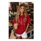 A woman stands in a market stall wearing a red oversized graphic T-shirt with three fish designs on the front, paired with white shorts and holding an iced coffee.