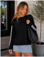 A woman wearing a black long-sleeve sweatshirt with white stripes down the sleeves, paired with a light blue denim mini skirt and carrying a black tote bag.