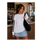 A woman in a cafe setting wearing a white long-sleeve sweatshirt with black stripes down the sleeves, paired with a light blue denim skirt and carrying a black shoulder bag.