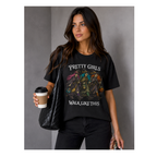 A woman modeling a black graphic t-shirt with the text 'PRETTY GIRLS WALK LIKE THIS' and a colorful illustration of three girls. She is holding a black quilted shoulder bag and a coffee cup against a gray background.