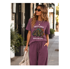 A woman modeling a matching mauve purple lounge set consisting of a graphic t-shirt and sweatpants, walking on a city sidewalk.