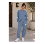 A woman stands outdoors wearing a matching dusty blue sweatshirt and jogger pants set with white star details on the sleeves and legs, paired with white sneakers.